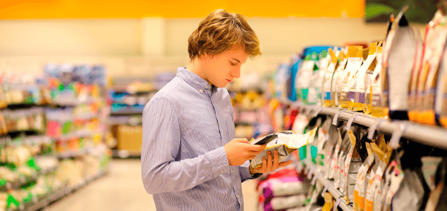 Boy shopping for pet food in the aisle of a supermarket, checking the labels on the packaging and discovering the ingredients.